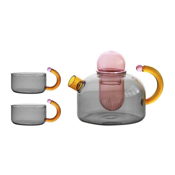 Glass teapot with pink interior and orange handles, accompanied by two gray mugs with orange handles on a white background.