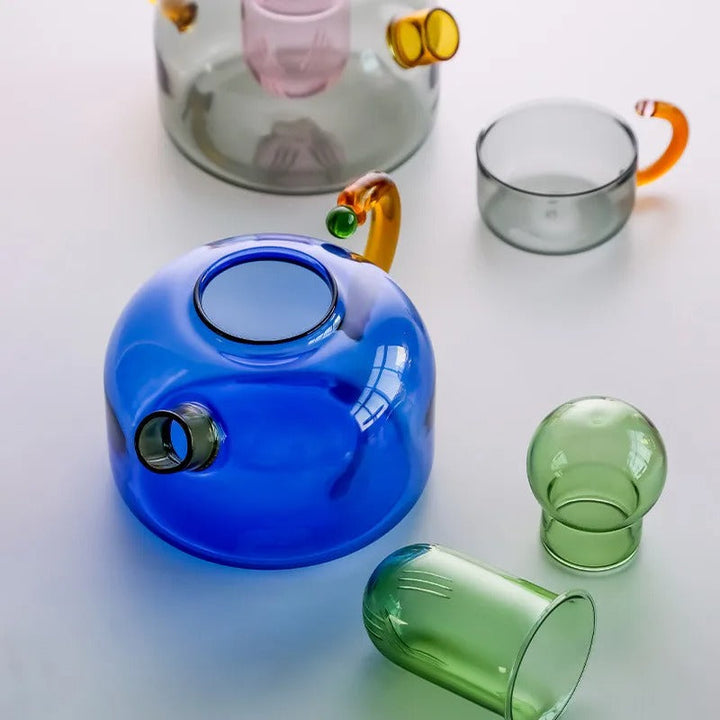 Colorful glass teapot and cups on a light background