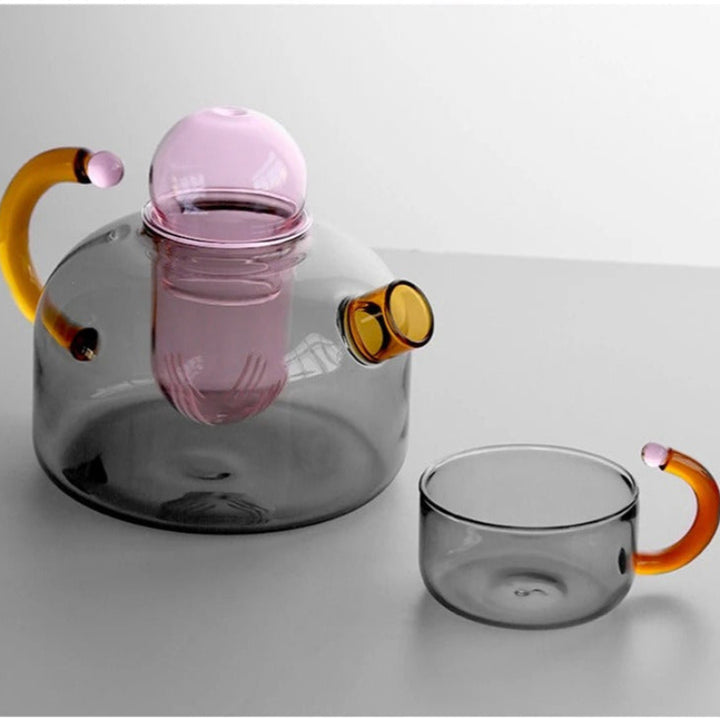 Glass teapot and mug with colorful handles on a light gray background