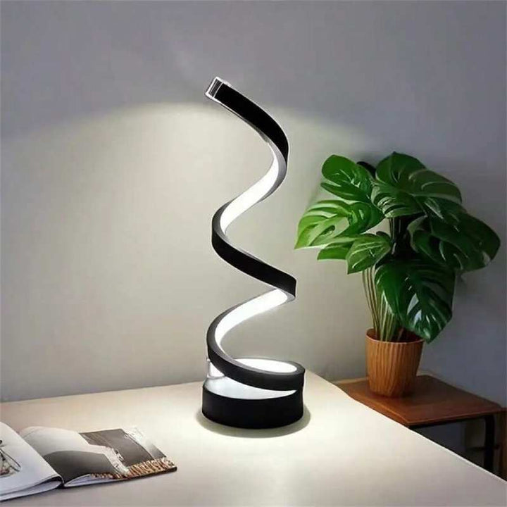 Modern spiral LED table lamp with white light beside potted plant, minimalist interior decor.