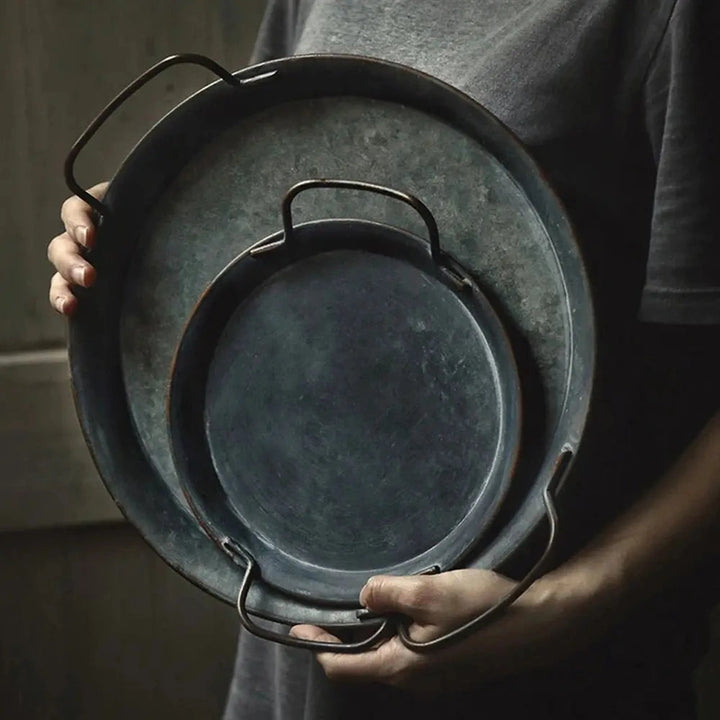 Person holding a stack of metal trays with an earthy, distressed tone, adding timeless character to home décor.