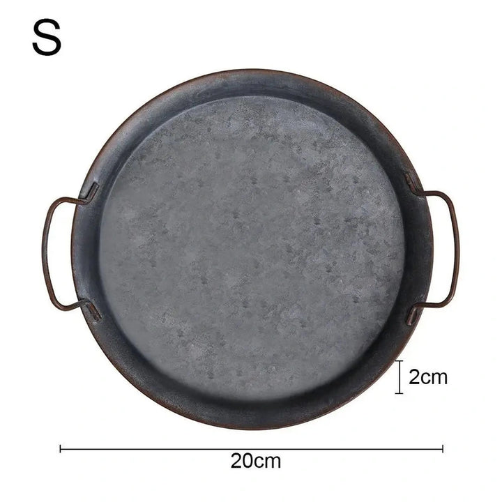 Close-up of a small, round vintage metal tray with detailed distressed finish and handles.