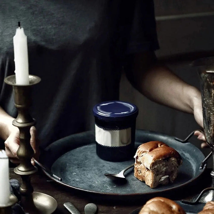 Person holding the large metal tray with bread and a jar, candle in the background