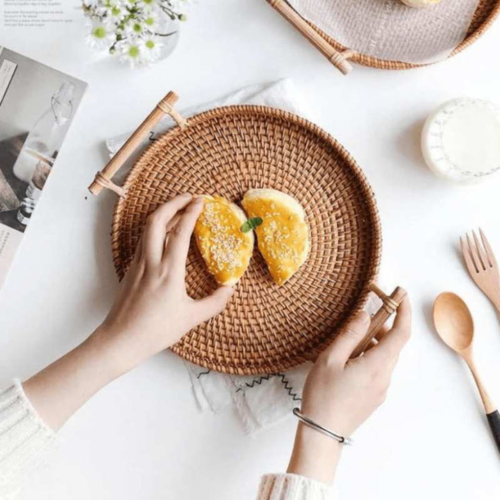 Handwoven rattan tray with handles used for serving pastry on white table in minimalist home setting
