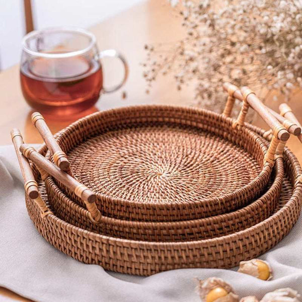 Stack of handcrafted rattan serving trays with wooden handles on table beside tea cup in cosy home décor