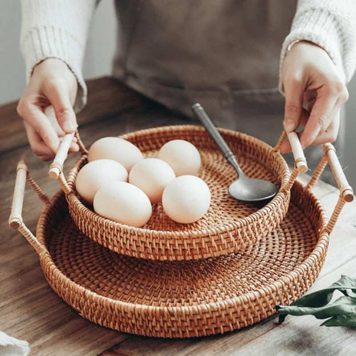 Person holding round rattan serving tray with handles filled with fresh eggs in Nordic kitchen setting