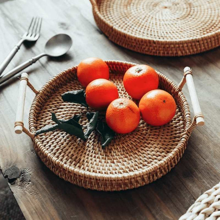 Handwoven rattan serving tray with oranges on wooden dining table, minimalist Scandinavian home accessory