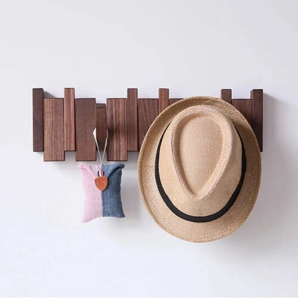 Wooden wall hook holding a straw hat and two small bags on a white background