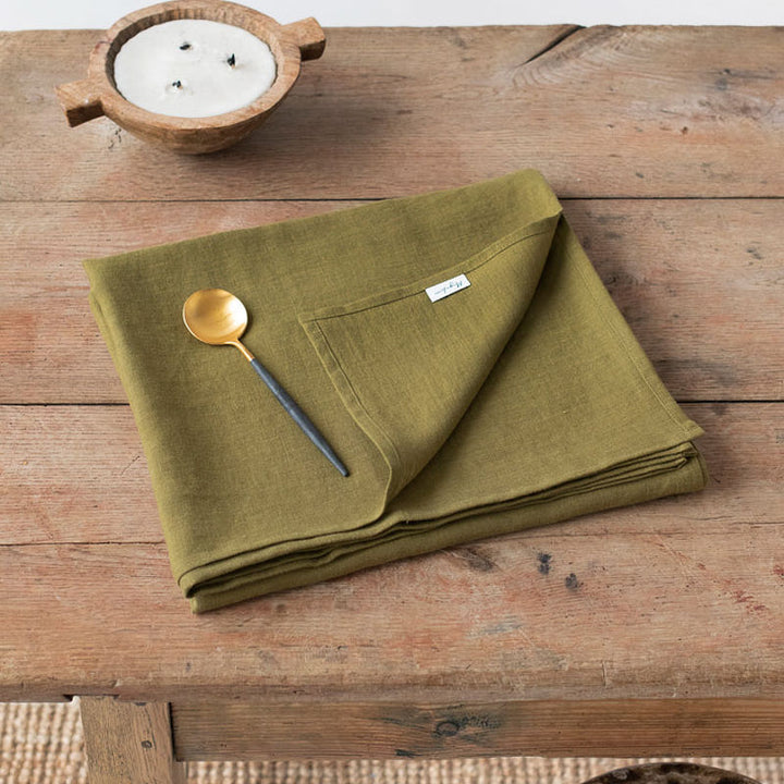 Warm-brown- folded linen tablecloth on a wooden table with a spoon and small bowl.