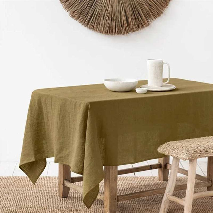 Warm-brown linen tablecloth on a wooden table with a white wall and decorative item in the background