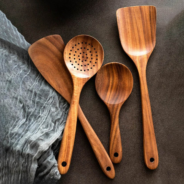 Teak wood spatulas and cooking spoons laid out on dark kitchen surface, handmade Nordic utensils