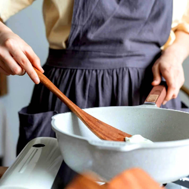 Hand stirring food in ceramic pan using wooden spatula, eco kitchen utensil with ergonomic grip