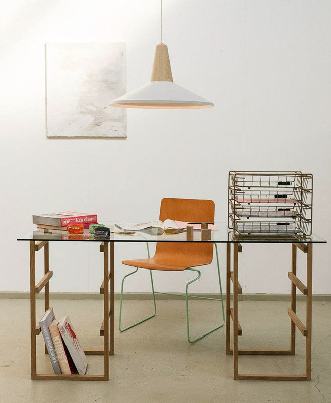 Modern glass desk with wooden frame, orange chair, and books in a minimalistic room.