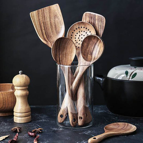 Set of wooden kitchen utensils in a glass holder on a dark surface with a black background.