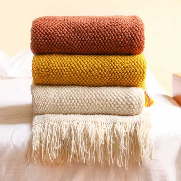 Stacked acrylic waffle-knit blankets in orange, mustard, cream and beige with tassel fringe for Scandinavian home décor
