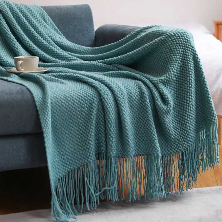 Light teal acrylic waffle-knit throw with tassel fringe draped casually over a sofa for calm Nordic styling