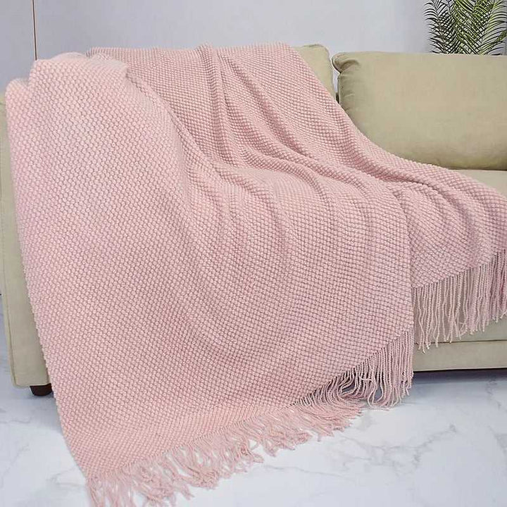 Soft pink acrylic waffle-knit throw with tassel fringe draped over a beige sofa for cosy minimalist home décor