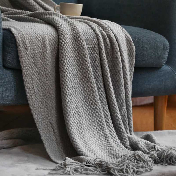 Light grey acrylic waffle-knit throw with textured tassel fringe styled on a blue armchair for modern Scandinavian interiors
