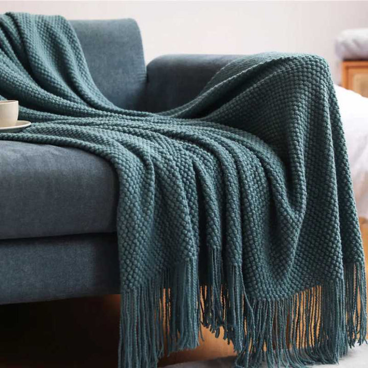Teal acrylic waffle-knit throw with tassel fringe draped over a sofa for cosy Scandinavian living room décor