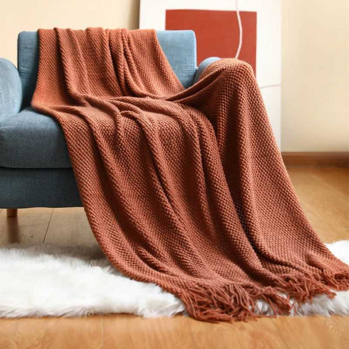 Rust orange acrylic waffle-knit throw with tassel fringe styled on an armchair for warm Nordic home accents