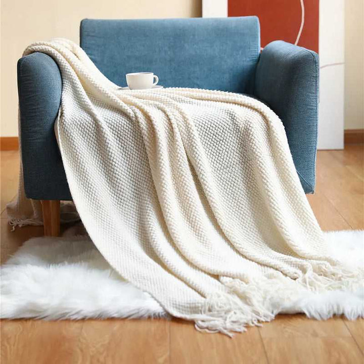 White acrylic waffle-knit throw with soft tassel fringe draped over a blue armchair for minimalist bedroom décor