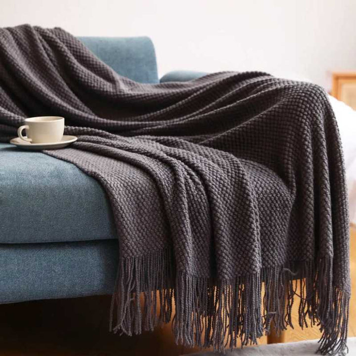 Charcoal grey acrylic waffle-knit throw with long tassel fringe draped over a sofa for modern home styling