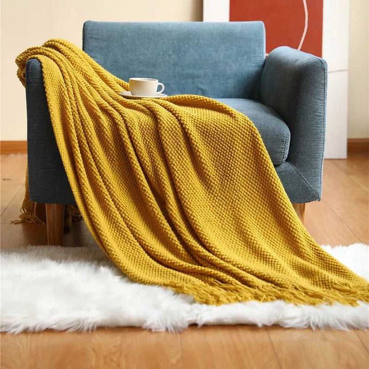 Mustard yellow acrylic waffle-knit throw with tassel fringe styled on an armchair for bright Scandinavian décor