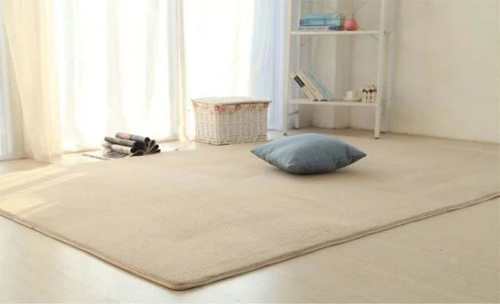 Beige rug with a pillow on a light-colored floor in a room with a shelf and curtains.