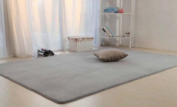 Gray rug on a wooden floor with a pillow and small shelf in the background