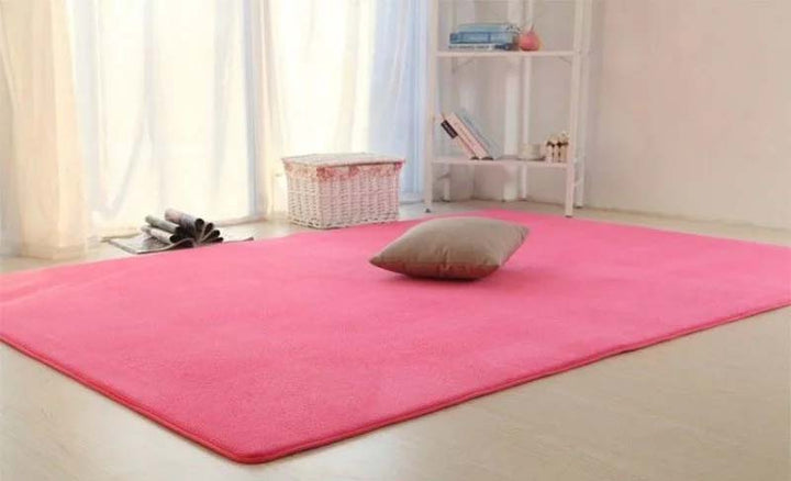 Pink rug with a pillow on a light-colored floor in a room with white walls and a window.