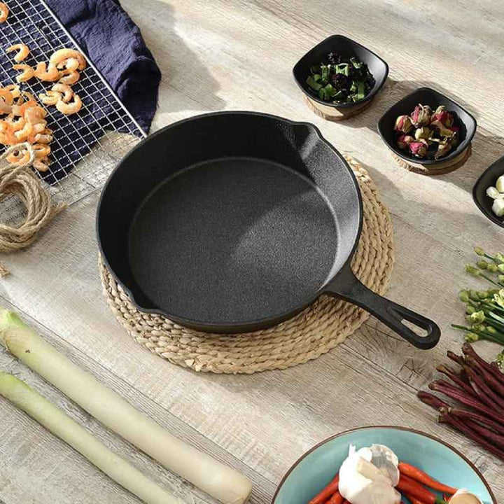 Cast iron skillet placed on a woven mat surrounded by fresh ingredients on a wooden table.