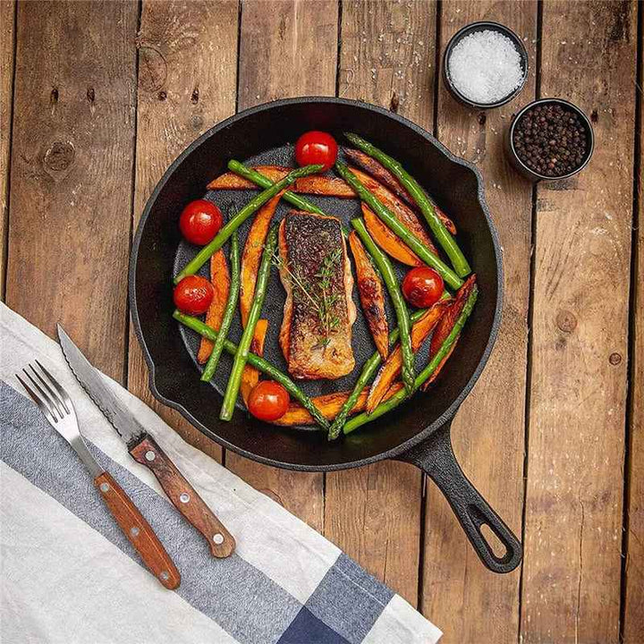 Cast iron skillet frying salmon, tomatoes and vegetables for even-heat stovetop cooking.