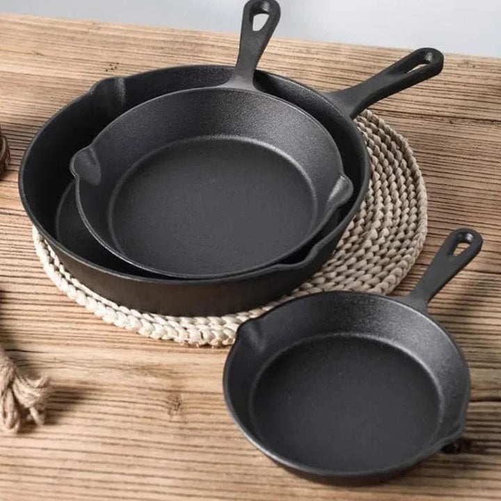 Three cast iron skillets nested on a table, showing heavy-duty design for sautéing and frying.