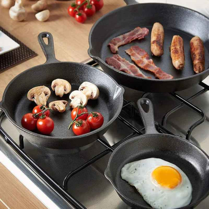 Cast iron skillets cooking bacon, eggs and vegetables, showing even heat retention on a gas stove.