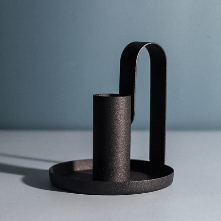Scandinavian black candle holder in brushed iron with soft shadow on blue tabletop