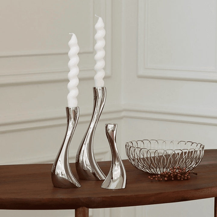 Curved ceramic candle holders with white spiral candles on wooden table in modern interior