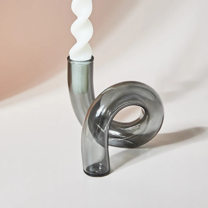 Modern smoke grey glass loop candle holder with white spiral taper candle on minimalist beige background