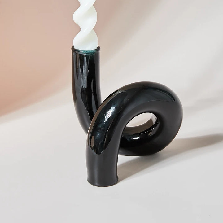 Black glass curved loop candle holder with white spiral taper candle on modern neutral background