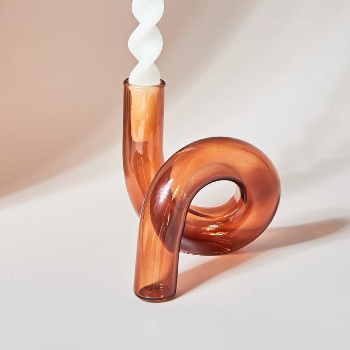 Amber curved glass candle holder with white spiral taper candle in minimalist Scandinavian decor setting