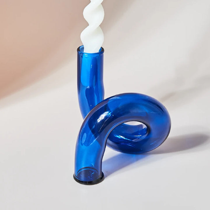 Deep blue glass curved candle holder with white twisted taper candle on neutral background