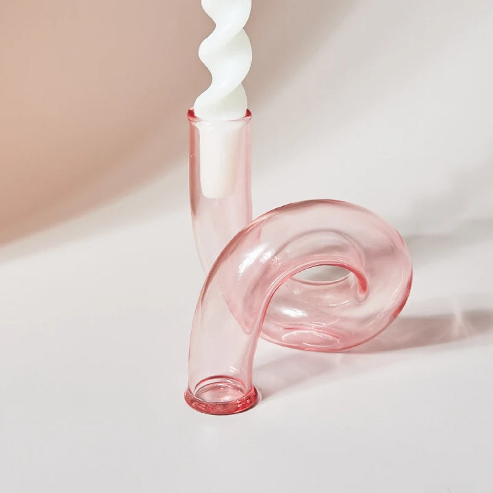 Soft pink glass curved candle holder with white spiral taper candle in modern minimalist style