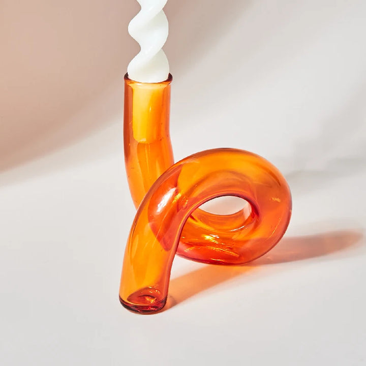 Vibrant orange glass curved candle holder with white twisted taper candle on light background