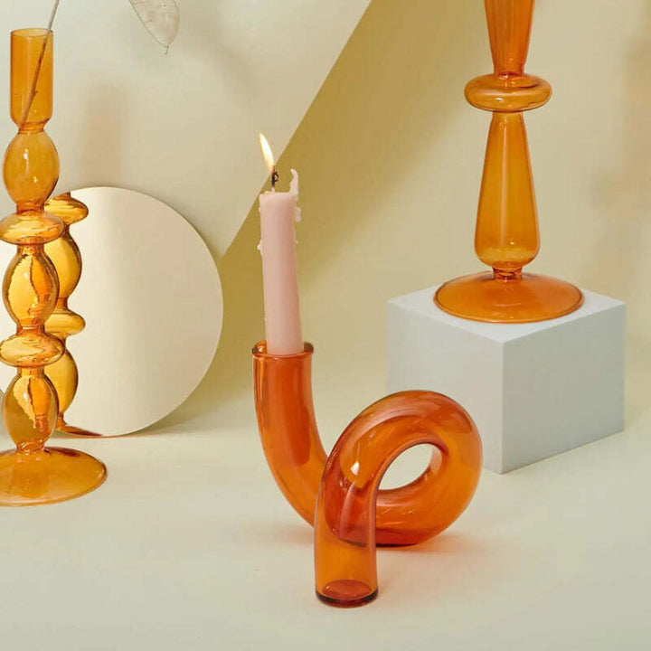 Amber curved glass candle holder with pink taper candle styled with matching glass decor in warm lighting