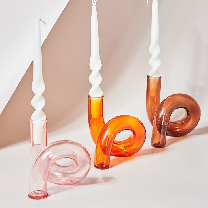 Curved pink, orange, and amber glass candle holders with white twisted taper candles on minimalist backdrop