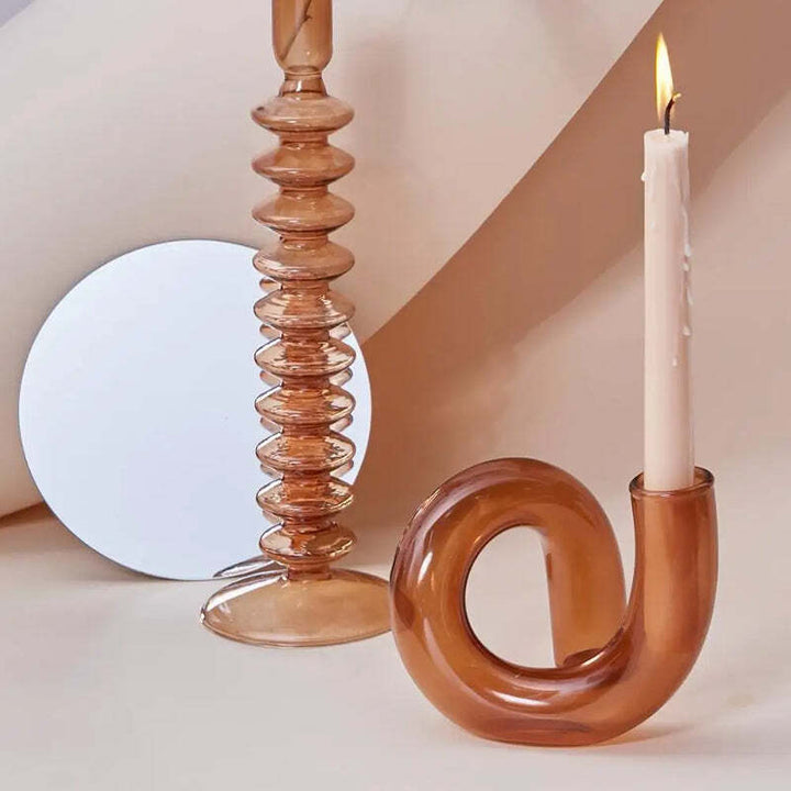 Amber glass swirl candle holder with white taper candle beside ribbed amber glass candlestick on neutral background