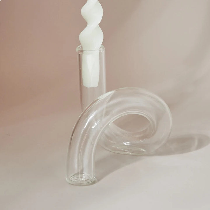 Elegant clear glass curved candle holder with white twisted taper candle on soft neutral background