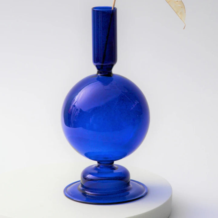 Cobalt blue glass round candle holder with tall neck and glossy finish styled with dried branch