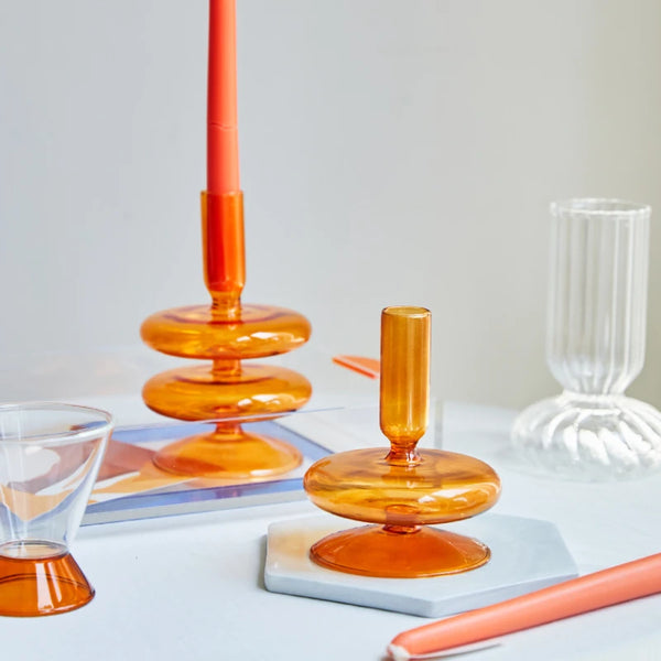 Amber glass candle holders in modern donut design with orange taper candle on marble and glass coasters