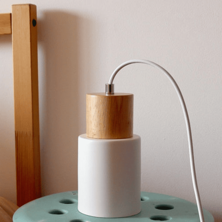 Close-up of white Nordic pendant lamp with natural wood detail and white cord, minimalist design.