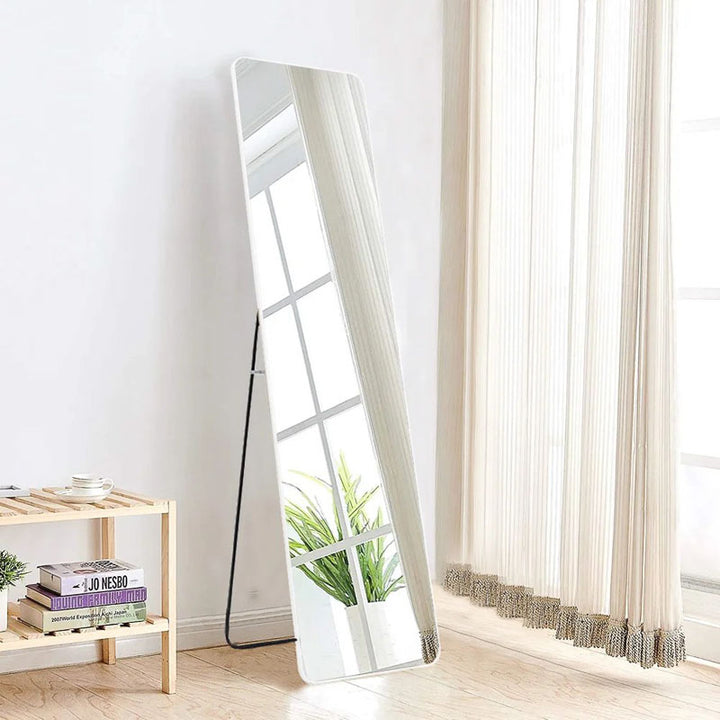 Tall mirror leaning against a wall in a room with a window and small table.